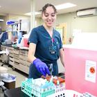 A medical worker in scrubs places a vial into a rack in a medical lab. 